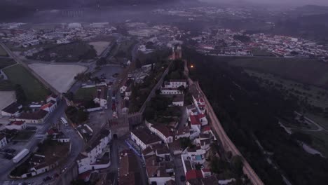 Tilt-up-shot-of-famous-town-Obidos-Portugal-with-low-clouds-during-sunrise,-aerial