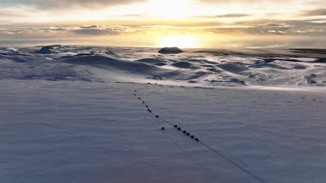 Aerial-panoramic-landscape-view-of-people-riding-snowmobiles-on-Myrdalsjokull-glacier-in-Iceland,-during-an-epic-sunset