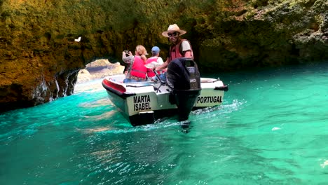 Close-up-shot-showing-guide-with-private-boat-visiting-famous-cliff-cave-of-Algarve-with-couple-of-tourist---slow-motion