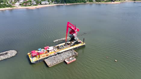 Toma-Aérea-De-Arriba-Hacia-Abajo-De-Una-Barcaza-Industrial-Con-Grúa-Montada,-Levantando-Rocas-En-El-Río-De-La-Bahía-Durante-El-Día-Soleado---Staten-Island,-Nueva-York