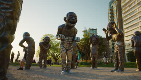 People-enjoying-Laughing-Statues-at-Morton-Park,-Vancouver,-during-golden-hour