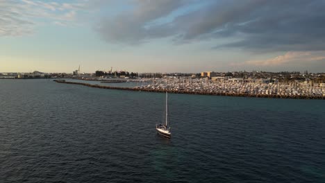 Drone-shot-showing-sailing-boat-arriving-Fremantle-Fishing-Boat-Harbour-at-sunset,-Western-Australia