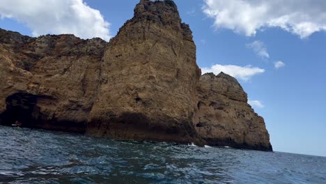 Wide-shot-of-gigantic-rocky-cliff-coastline-at-Algarve-with-wavy-ocean-water---pov-shot-from-boat