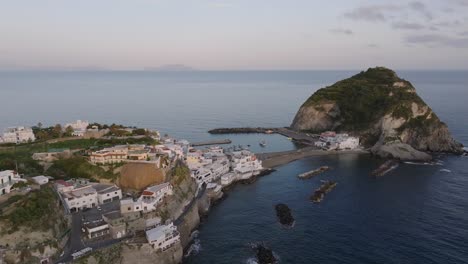 Sea,-islet-and-houses-on-seaside-cliffs-at-Ischia-in-Italy,-aerial-pan