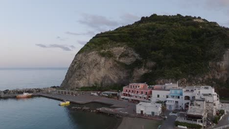 Forward-tilt-up-aerial-of-houses,-beach-and-islet-by-coast-of-Ischia