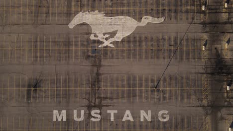 Empty-Parking-lot-of-the-Flat-Rock-Assembly-plant-with-the-Mustang-logo-painted-on-it,-Aerial-ascending-Birds-Eye-view