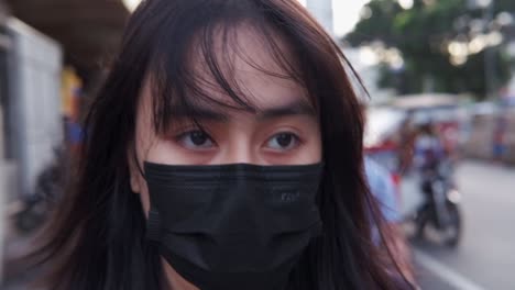 Close-up-dramatic-shot-of-a-distressed-Asian,-black-haired-woman-in-a-face-mask-walking-through-the-streets-of-Manila,-Philippines