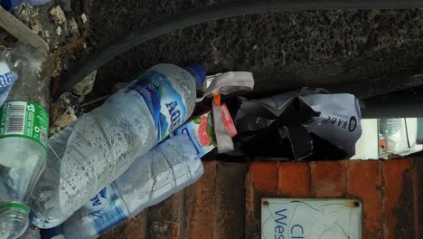 Vertical-Slow-motion-tilt-up-shot-of-trash-lying-around-due-to-lack-of-waste-management-on-Nusa-Penida-in-Bali-Indonesia-with-plastic-bottles,-plastic-bags-and-other-trash