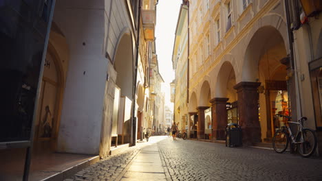 Quaint-cobblestone-street-with-arched-doorways-backlit-in-Bolzano,-Italy