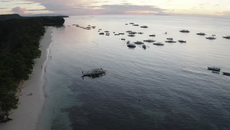 Filmische-Drohnenaufnahmen-Eines-Sandstrandes-Mit-Einem-Tropischen-Wald-Im-Hintergrund-Und-Booten-Auf-Dem-Ruhigen-Wasser-Bei-Sonnenuntergang,-Luftaufnahmen,-Philippinen,-Asien