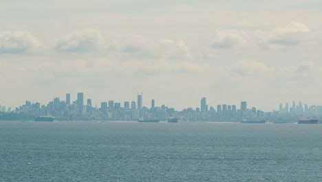 Vancouver-City-Skyline-view-from-English-Bay,-Cargo-vessels-in-foreground
