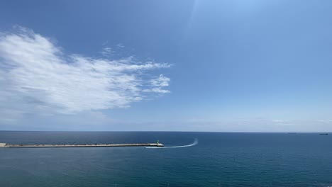 Vista-Panorámica-Del-Océano-Con-El-Cielo-Brillante-Y-Un-Barco-Que-Entra-En-Un-Puerto