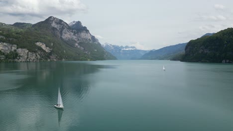 Sailboat-riding-on-lake's-surface-with-mountains-behind