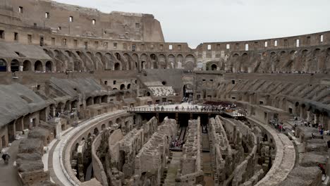 Una-Toma-Panorámica-Mirando-Hacia-Abajo-En-La-Espectacular-Arena-Interior-Del-Coliseo,-Paredes-Altas-Y-Arcos-Rodean-El-Icónico-Anfiteatro-En-Roma,-Italia