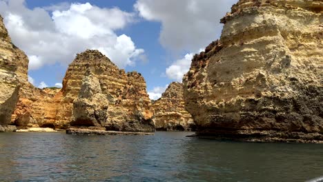 Wide-shot-showing-stunning-sandstone-cliff-formation-of-algarve-during-boat-trip-on-atlantic---puffy-clouds-at-sky-in-background