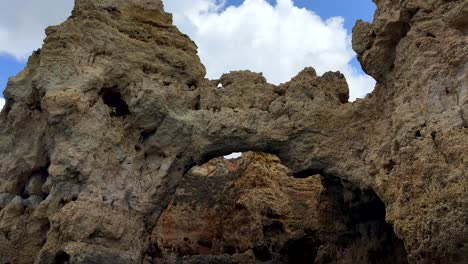 Von-Unten-Nach-Oben-Geschossene-Sandsteinklippenformation-Mit-Verschiedenen-Höhlen-Und-Gipfeln-An-Der-Algarve-Vor-Wolken-Am-Himmel---Nach-Unten-Geneigte-Sicht-Vom-Boot-Aus