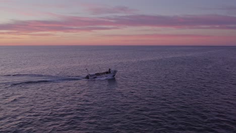 Small-boat-is-cruising-on-atlantic-ocean-near-Albufeira-at-sunrise,-aerial