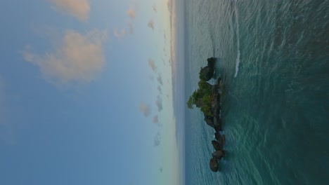 Vertical-fpv-aerial-under-rock-formation-in-the-Caribbean,-picturesque-sunset