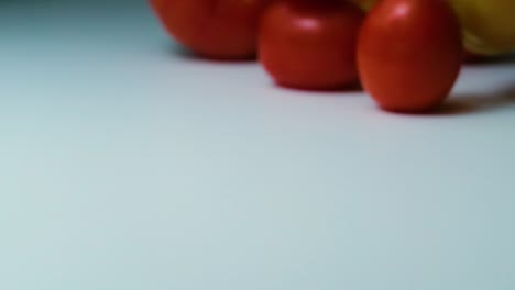 Slow-Motion-Shot-of-a-Variety-of-Tomatoes-Spilling,-Rolling-and-Bouncing-on-a-White-Surface