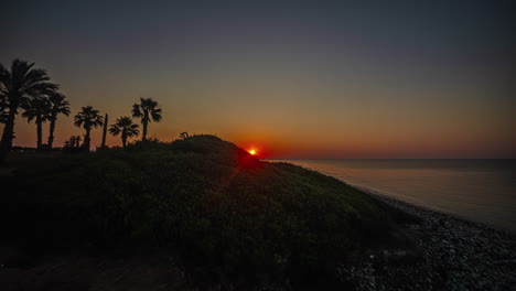Sunrise-over-rocky-ocean-shoreline-with-red-orange-ball-sun-rising,-paphos-Cyprus