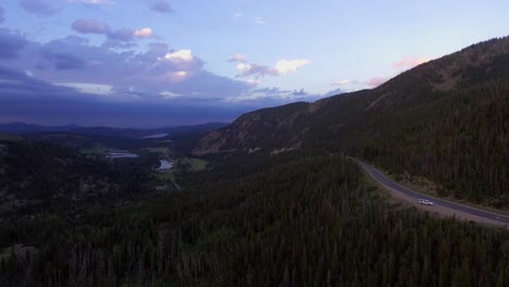 Aerial-of-Road-Leading-Down-Mountain,-Aerial-View-of-Colorado-Landscape-During-Sunset,-Road-Through-Rocky-Mountains-Leading-to-Reservoir