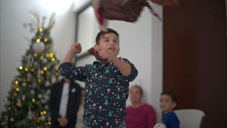 Niño-Latino-Joven-Con-Una-Camisa-Golpeando-Ferozmente-Una-Piñata-De-Reno-Marrón-Con-El-Puño