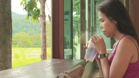 Vista-Lateral-Primer-Plano-De-Una-Mujer-Tailandesa-Bebiendo-Un-Refresco-En-Un-Café-Con-Jardín-En-Khao-Yai,-Tailandia
