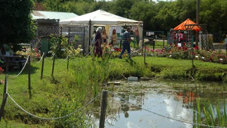 People-visit-a-rose-plants-garden-fest-at-the-plant-nursery-in-summer-and-admire-the-blooming-roses-grown-at-the-pond-edge