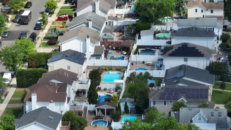 Aerial-orbit-shot-of-american-residential-area-with-swimming-pools-in-garden-And-driving-cars-on-road-during-sunny-day-in-summer---Installed-solar-panels-on-roof-producing-green-energy