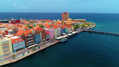 4k-cinematic-drone-shot-of-stunning-UNESCO-buildings-of-the-Handelskade-in-Willemstad-City,-being-revealed-by-cloud-shadow-and-bright-sunlight