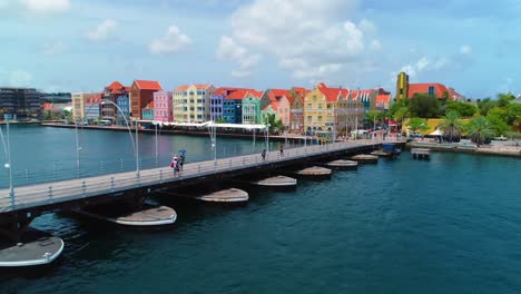 Toma-De-Drones-Cinematográficos-De-4k-Del-Puente-Flotante-De-Pontones-De-La-Reina-Emma,-Con-Coloridos-Edificios-De-La-Unesco-En-El-Fondo-En-Willemstad,-Curacao