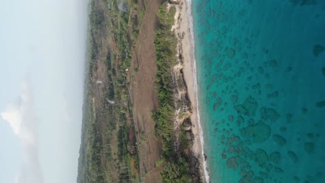 Vertical-drone-shot-of-beautiful-transparent-lagoon,-sandy-beach-and-scenic-landscape-in-background