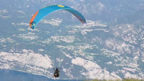 Female-paraglider-take-off-from-monte-Baldo-and-fly-above-Garda-lake-with-mountain-background,-Italy