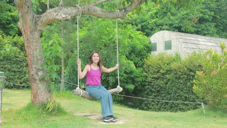 Junge-Schöne-Thailändische-Frau-Schwingt-Auf-Einer-Seilschaukel-In-Einem-Garten