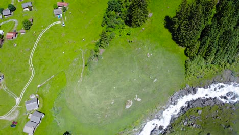 Bird’s-eye-view-above-peaceful-mountain-village-by-roaring-stream,-Switzerland