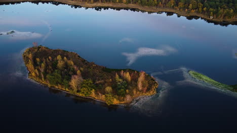 Lake-island-with-forest-and-water-reflecting-sky-colors,-aerial-orbit-view