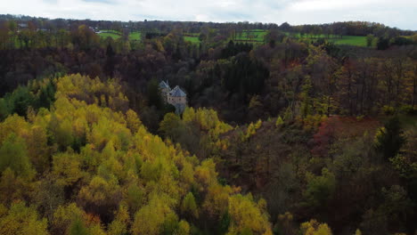 Castle-tower-hiding-between-trees-of-autumn-forest,-aerial-drone-view