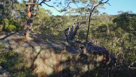 Indigenous-Australian-girl-walking-out-onto-a-large-rock,-overlooking-the-bush-below