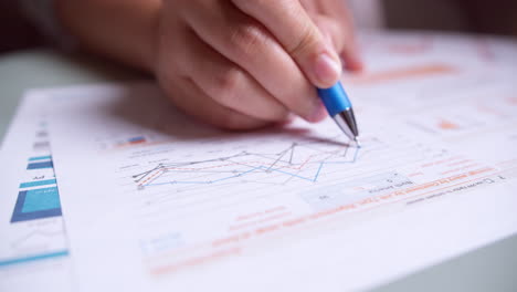 Close-up-of-businesswoman's-hands-with-pen-working-at-office-desk-and-analyzing-graphs-and-charts,-profit-report-checking
