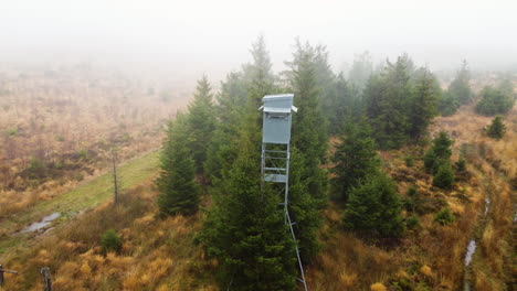 Metal-hunting-tower-hiding-in-mystical-foggy-landscape,-aerial-drone-view