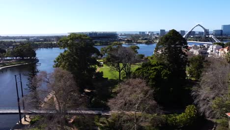 Vista-Aérea-De-Drones-Viajando-Lateralmente-Sobre-El-Parque-Costero-Del-Este-De-Perth-Con-El-Puente-Matagarup-Hasta-El-Puente-Peatonal-Colgante-Con-El-Estadio-Optus-Y-El-Río-Swan