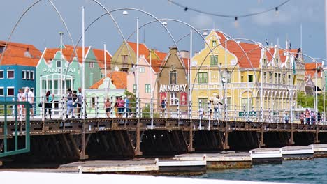 Paralaje-Cinematográfico-De-4k-60-Fps-Vuela-Por-El-Puente-Flotante-Reina-Emma-Con-Turistas-Y-Peatones-Caminando-Sobre-él,-En-La-Ciudad-De-Willemstad,-Curazao