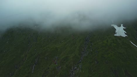 Grüne-Berge-Mit-Roten-Seilbahnkabinen,-Die-In-Die-Wolken-Hinein--Und-Wieder-Herausfahren