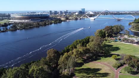 Drone-Aerial-View-over-Optus-Stadium-rotating-to-fly-over-East-Perth-Redevelopment-and-suspension-bridge-in-Claisebrook-Cove-with-Perth-skyline-in-background-and-in-Perth,-Western-Australia