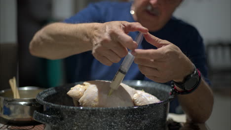 Close-up-of-the-hands-of-an-hispanic-man-injecting-a-raw-turkey-inside-a-pot-for-christmas-new-year-thanksgiving-celebrations