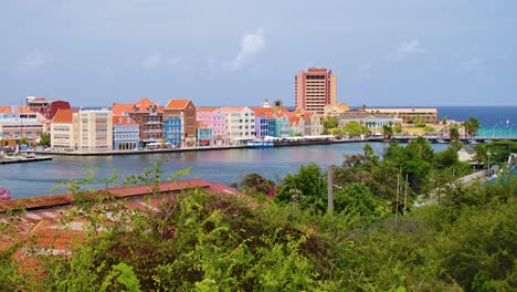 Slow-left-to-right-orbit-pan-of-Willemstad-city-featuring-the-iconic-colorful-world-heritage-UNESCO-buildings-of-the-Handelskade-in-Punda,-Curacao