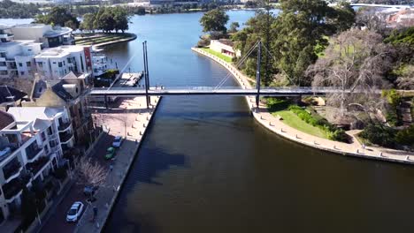 Vista-Aérea-De-Drones-Que-Se-Acerca-Hacia-Atrás-Sobre-La-Gente-Que-Camina-A-Lo-Largo-Del-Puente-Peatonal-Colgante-En-Claisebrook-Cove,-Perth-Este-Y-Río-Swan