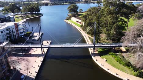 Vista-Aérea-De-Drones-Sobre-Personas-Caminando-A-Lo-Largo-Del-Puente-Peatonal-Colgante-En-Claisebrook-Cove,-East-Perth-Y-Swan-River