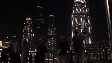 Gente,-Turistas,-Familias-Mirando-La-Fuente-De-Agua,-Espectáculo-De-Luces-En-El-Centro-Comercial-Dubai-Mall-En-El-Centro-De-Dubai,-Emiratos-Árabes-Unidos-Con-Rascacielos-Y-Edificios-Iluminados-Por-La-Noche.