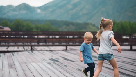 Little-girl-with-younger-brother-run-along-wooden-deck